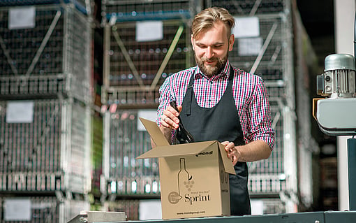 A man packing a wine bottle into a corrugated box.