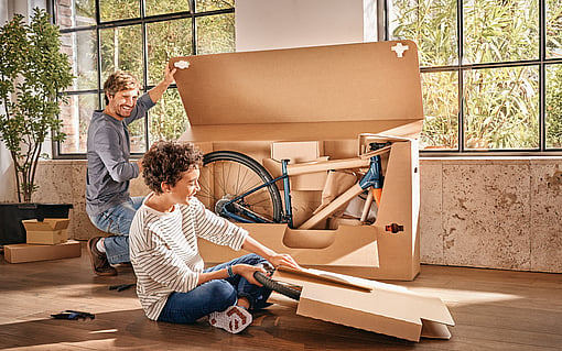 A man and a child unpacking a new bike from a cardboard box.
