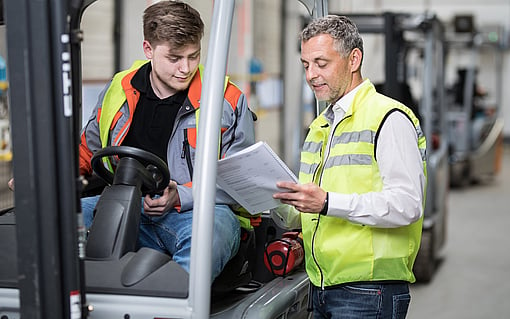 Two manufacturing colleagues reviewing a document beside a forklift.