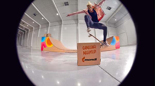 Olympic skateboarder Julia Bruckler performing an ollie over a carboard box with "challenge accepted" written on it and designed by Mondi.