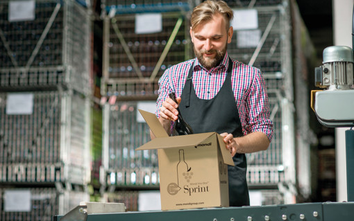 A man packing a wine bottle into a corrugated box.