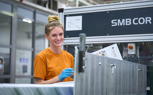 A woman smiling while working on a packaging manufacturing machine.