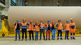 A few colleagues are standing in front of a paper roll and doing thumbs up towards the camera.
