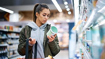 A young woman is reading a nutrition label while shopping.