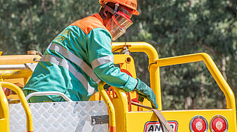 Worker with blue safety equipment and safety glasses is working on top of a yellow car.