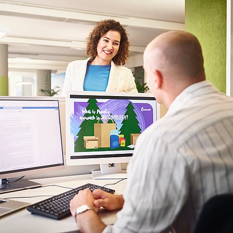 woman standing over a man's desk as he looks at a computer screen.