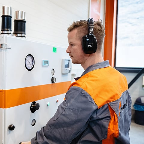 Production setting showing machinery in use, with an employee overseeing the process and a paper bag fitted to the system.