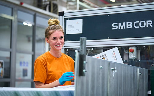 A woman smiling while working on a packaging manufacturing machine.