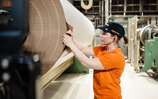 Worker in a manufacturing facility checking a large paper reel on production equipment.