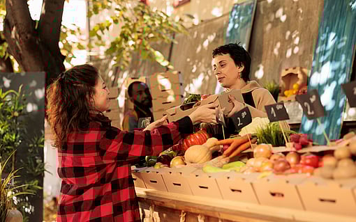 Women standing in front of selected fruit in corrugated boxes, buying fruit.