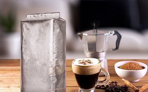 coffee packaging next to a cup of coffee, coffee grounds and coffee pot on wooden table