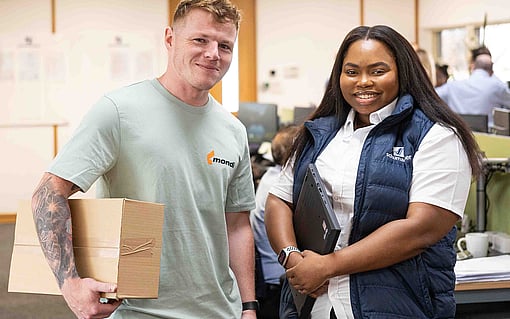 A man carrying a corrugated box and a woman smiling in an office space.