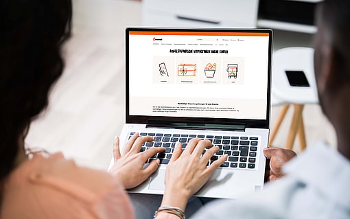 Two people sit together and view packaging-related content on a laptop. The screen displays product or packaging information, while both individuals focus on the computer in an office setting.