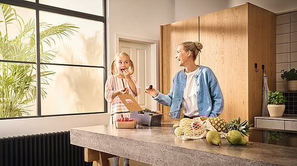 A mother handing her daughter fresh berries in the kitchen.