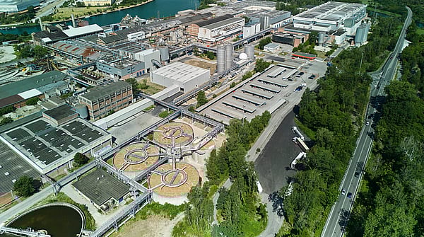 Aerial view of Mondi's Duino mill, located beside a canal and surrounded by green landscape.