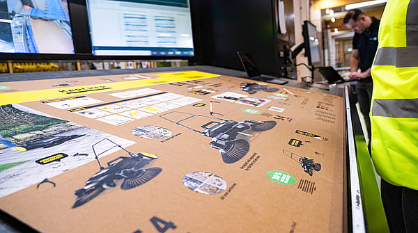 man in hi-vis jacket overlooking a machine printing imagery and text onto a cardboard box