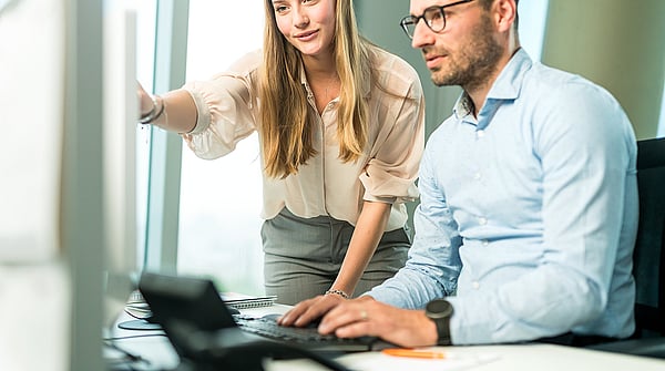 A man and a woman look closely at a computer screen; the woman points at it while both appear highly focused and engaged.