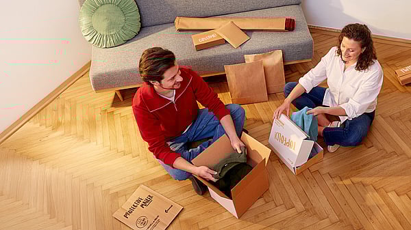 man and woman sitting cross legged opening corrugated packages