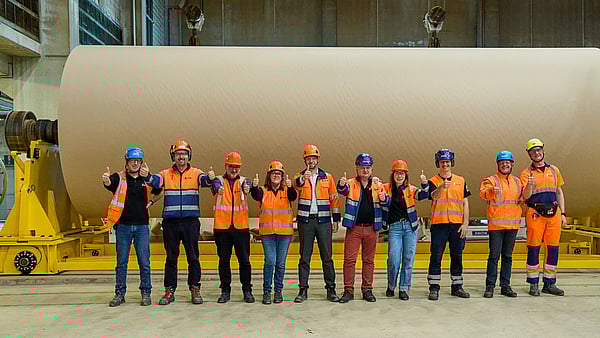 A few colleagues are standing in front of a paper roll and doing thumbs up towards the camera.