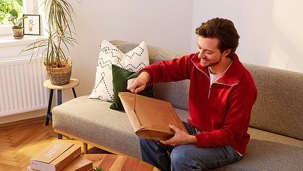 man in red jumper sitting on a sofa opening a package