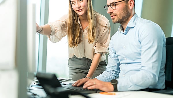 A man and a woman look closely at a computer screen; the woman points at it while both appear highly focused and engaged.