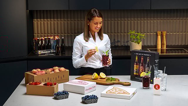 A woman in her kitchen with fresh produce and beverages.