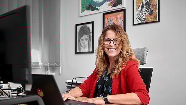 lady in red sweater sitting a t a desk with an open laptop in front of her