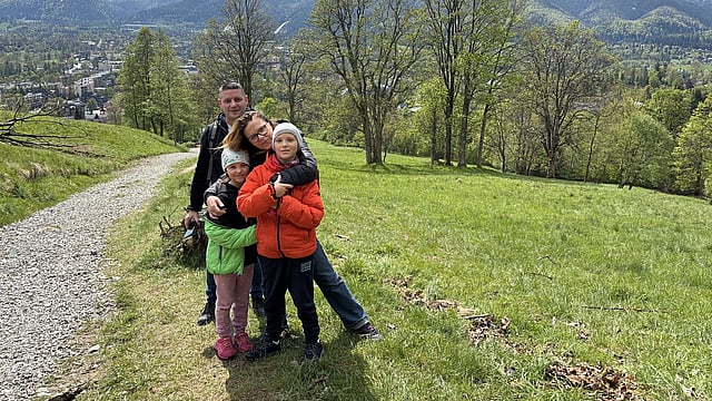family including man, woman and two children stand on a hillside with a town in the background
