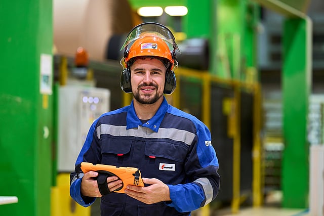 Männlicher Arbeiter in der Produktion mit Schutzausrüstung und iPad.