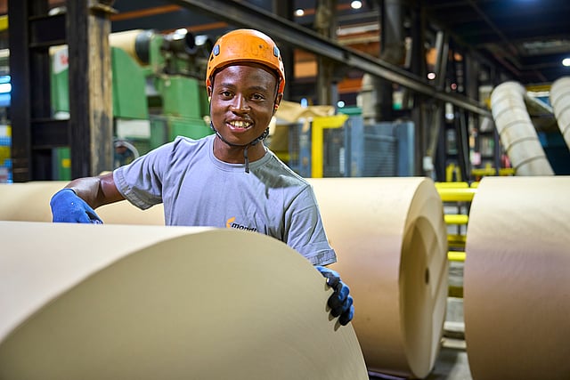 Mondi worker in a protective helmet and gloves handles large rolls of material inside an industrial production facility.