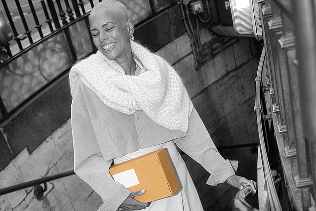 A black-and-white photo of a smiling woman with short hair in a suit, holding a Mondi package.