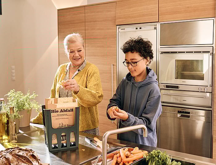 Two people preparing food together in a kitchen, with vegetables on a work surface.