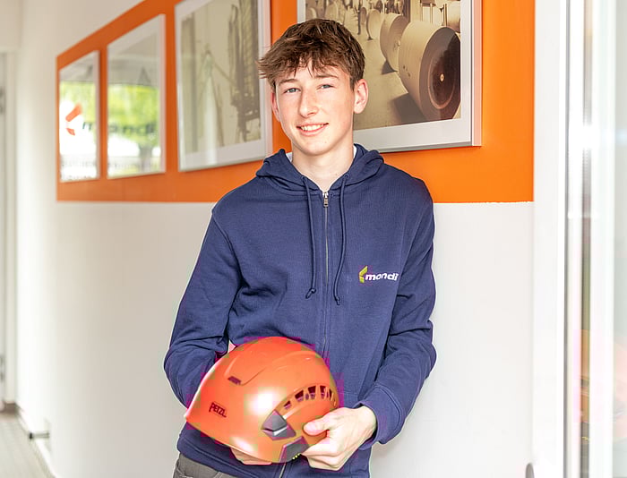 young boy in blue hoodie leaning against a wall while holding an orange hard hat