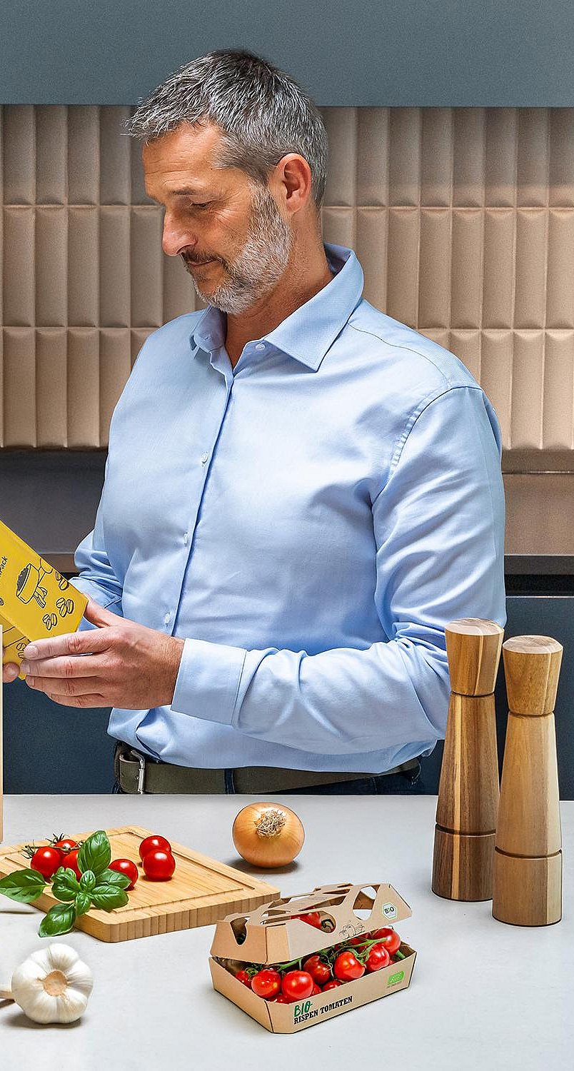 man standing at kitchen counter examining the wording on the back of some food packaging