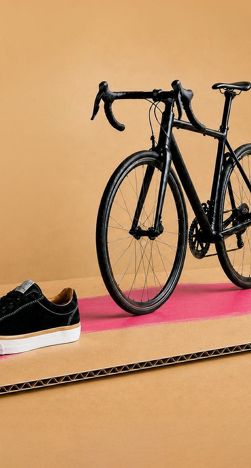 black bicycle, black shoe, apple and food pot on a piece of brown containerboard.