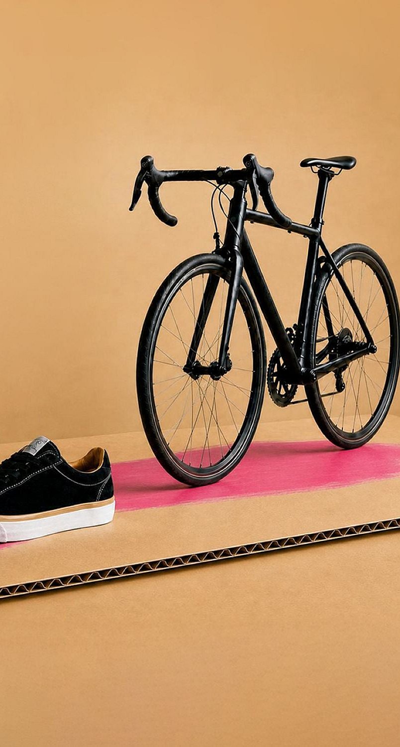 black bicycle, black shoe, apple and food pot on a piece of brown containerboard.