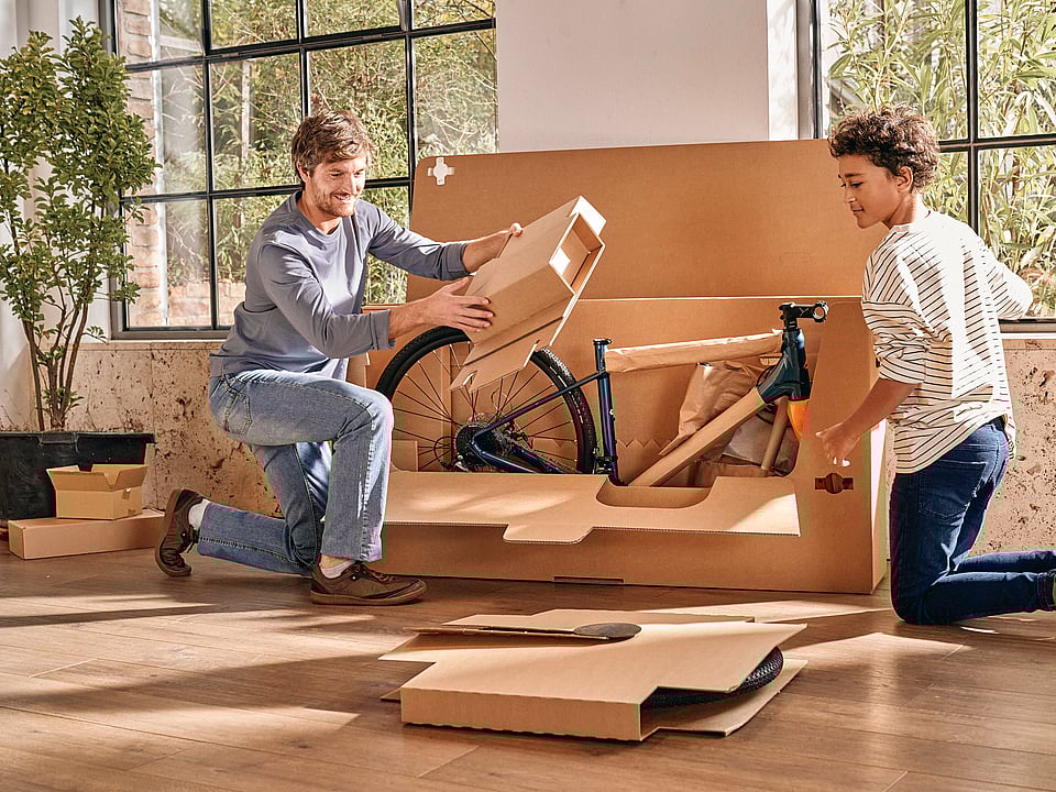 A man and a boy unboxing a bicycle from paper-based packaging.