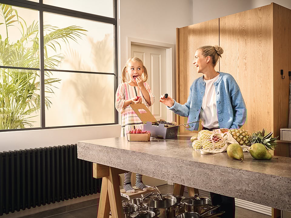 A woman and a child standing in a kitchen, laughing. On the kitchen counter, Mondi-branded corrugated packaging containing fresh fruit.