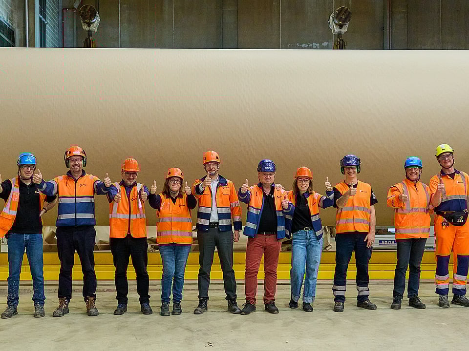 A few colleagues are standing in front of a paper roll and doing thumbs up towards the camera.