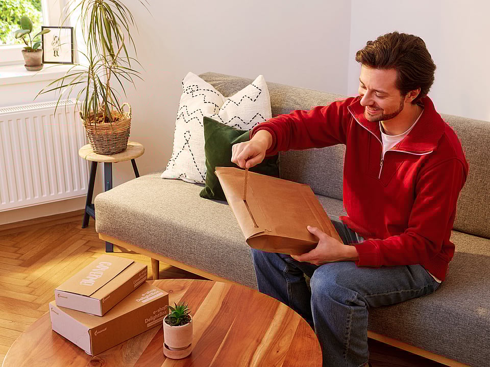A man sitting on a sofa opening a Mondi re/cycle MailerBAG.