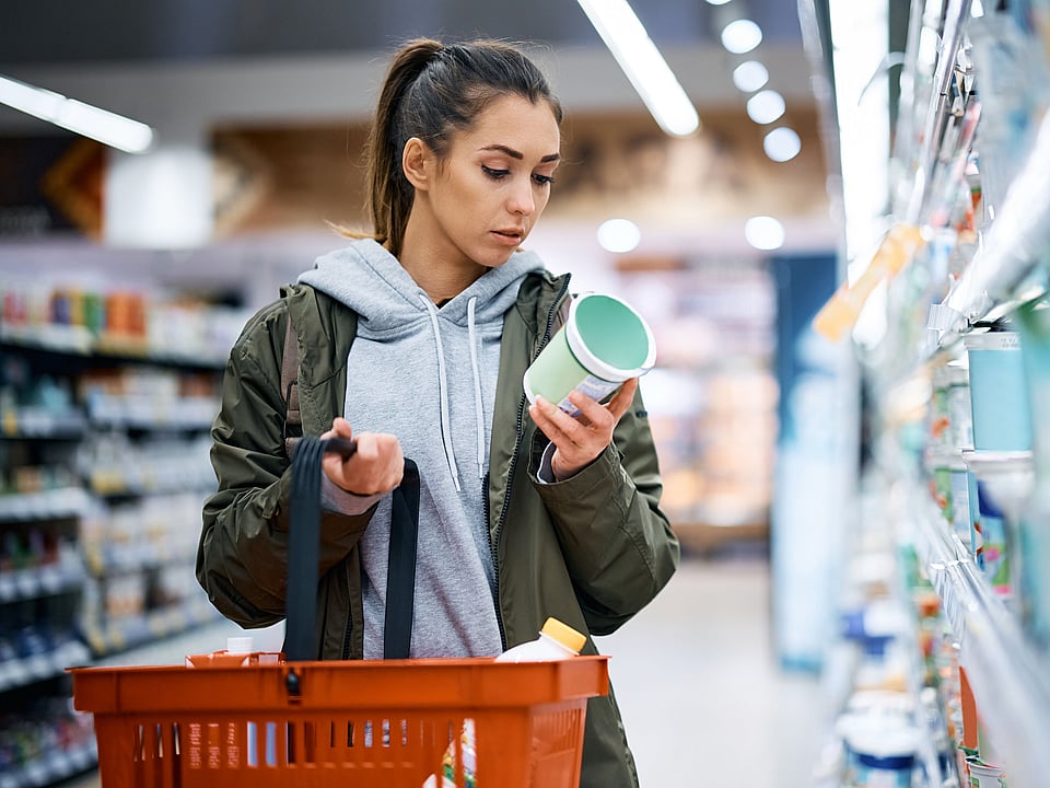 A young woman is reading a nutrition label while shopping.