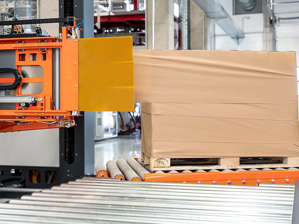 Automated stretch wrapping machine applying film around a palletized load in a warehouse.
