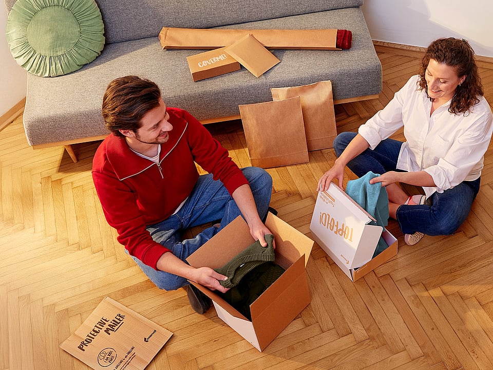 man and woman sitting cross legged opening corrugated packages