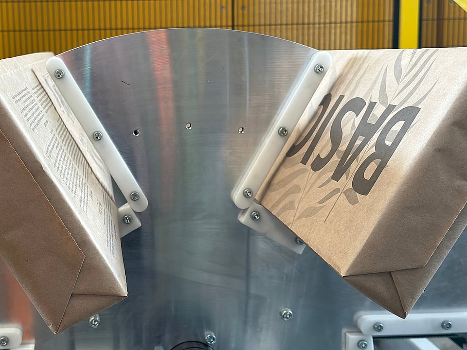 Paper bags moving through an industrial machine with a metal guiding mechanism during production.