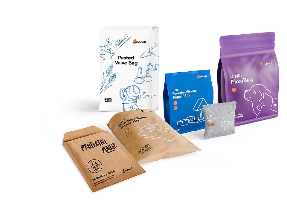 Collection of Mondi paper-based packaging solutions displayed on a light grey background, including a white pasted valve bag with blue illustrations, a blue stand-up pouch, a purple re/cycle FlexiBag pouch, a brown FunctionalBarrier paper pouch, a brown protective paper mailer, and a small grey sachet. The packaging features sustainability-focused branding, line drawings, and re/cycle product labels.