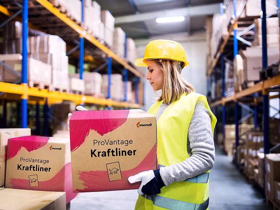 A woman in a warehouse holding a corrugated box with the words ProVantage Kraftliner written on it.c