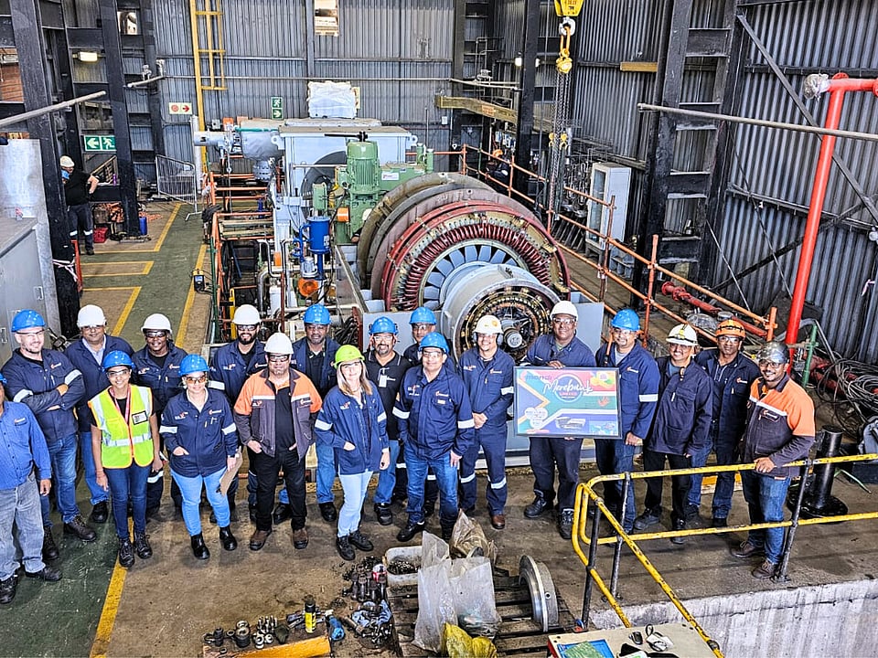 large group of people pose in front of factory machinery wearing hi-viz and blue jackets and hard hats