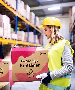 A woman in a warehouse holding a corrugated box with the words ProVantage Kraftliner written on it.c
