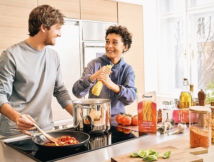 Two adults preparing food together in a kitchen with packaged ingredients on the counter.