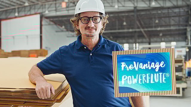 A man smiling and leaning against a stack of corrugated sheets. A sign on the right says ProVantage Powerflute.